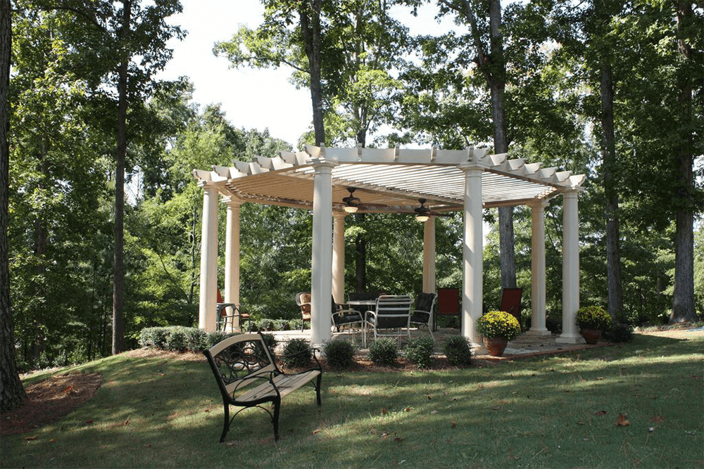 An ornate pergola in a lightly wooded setting.